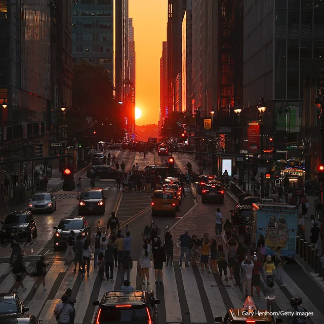 People stand on 42nd Street as they photograph the Manhattanhenge sunset in New York City.