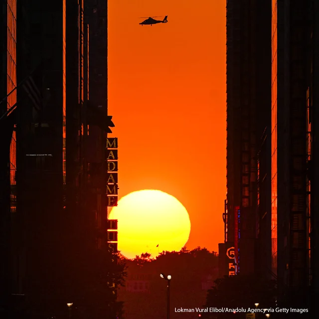 People stand on 42nd Street as they photograph the Manhattanhenge sunset in New York City.